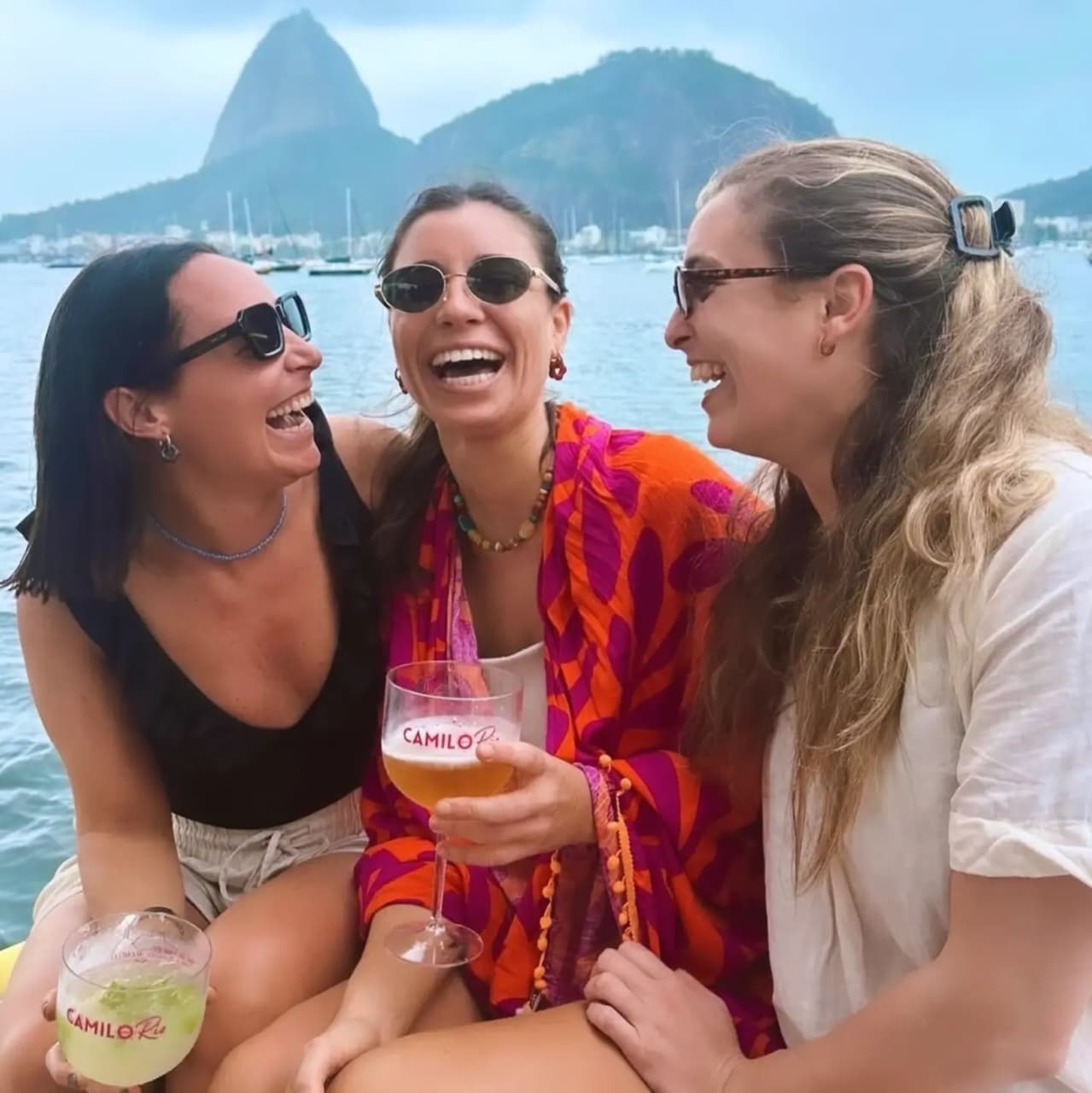 Amigas brindando con las copas de Camilo en Río a bordo de la lancha, con el Pão de Açúcar de fondo