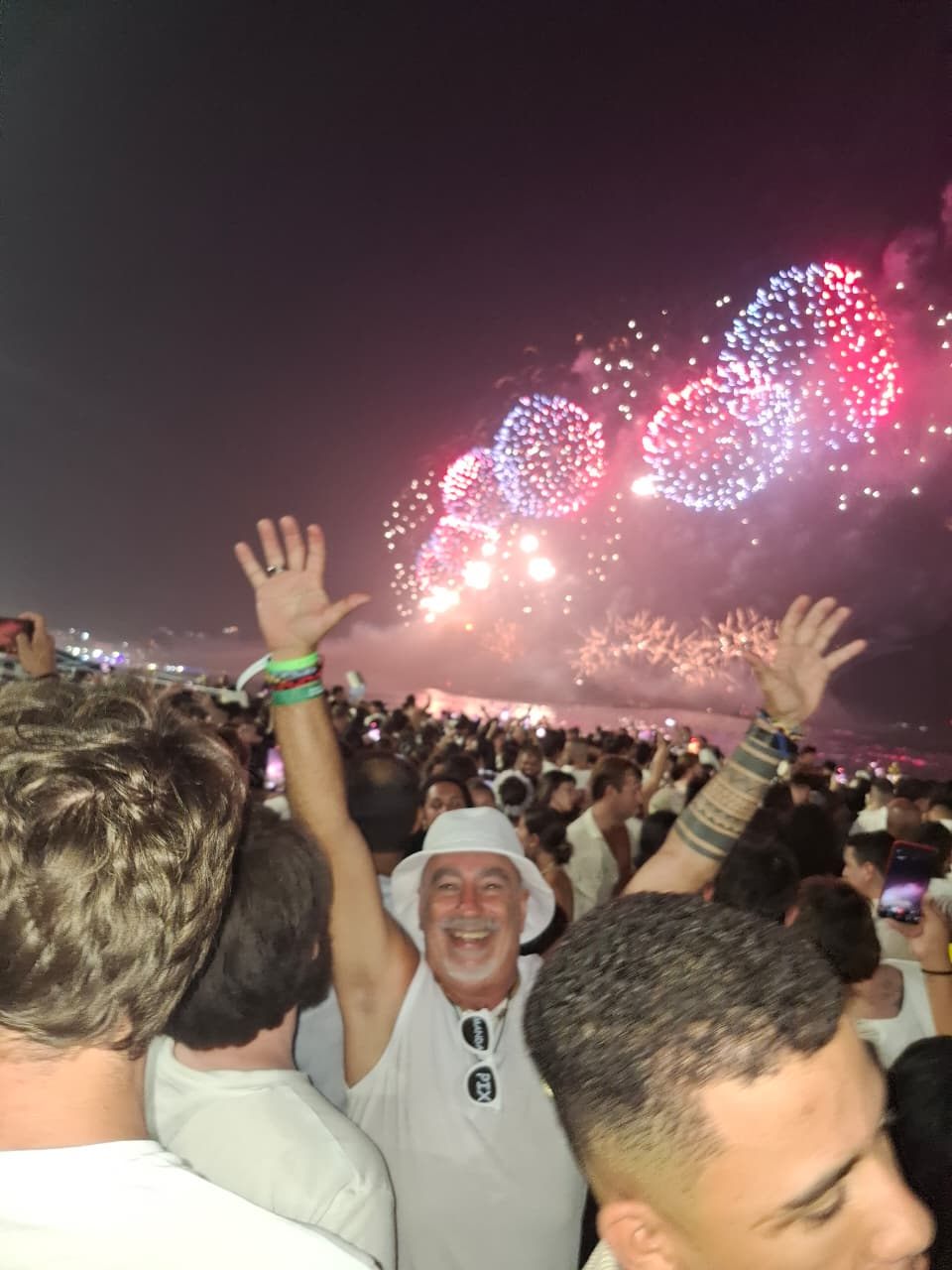 Fuegos artificiales del Réveillon de Copacabana sobre el mar, gente de blanco con los brazos en alto